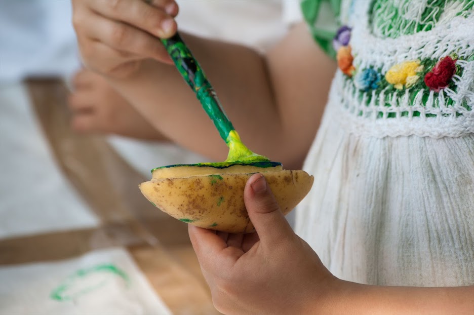 Ein Kind bemalt eine halbe Kartoffel mit grüner Farbe für einen Kartoffeldruck