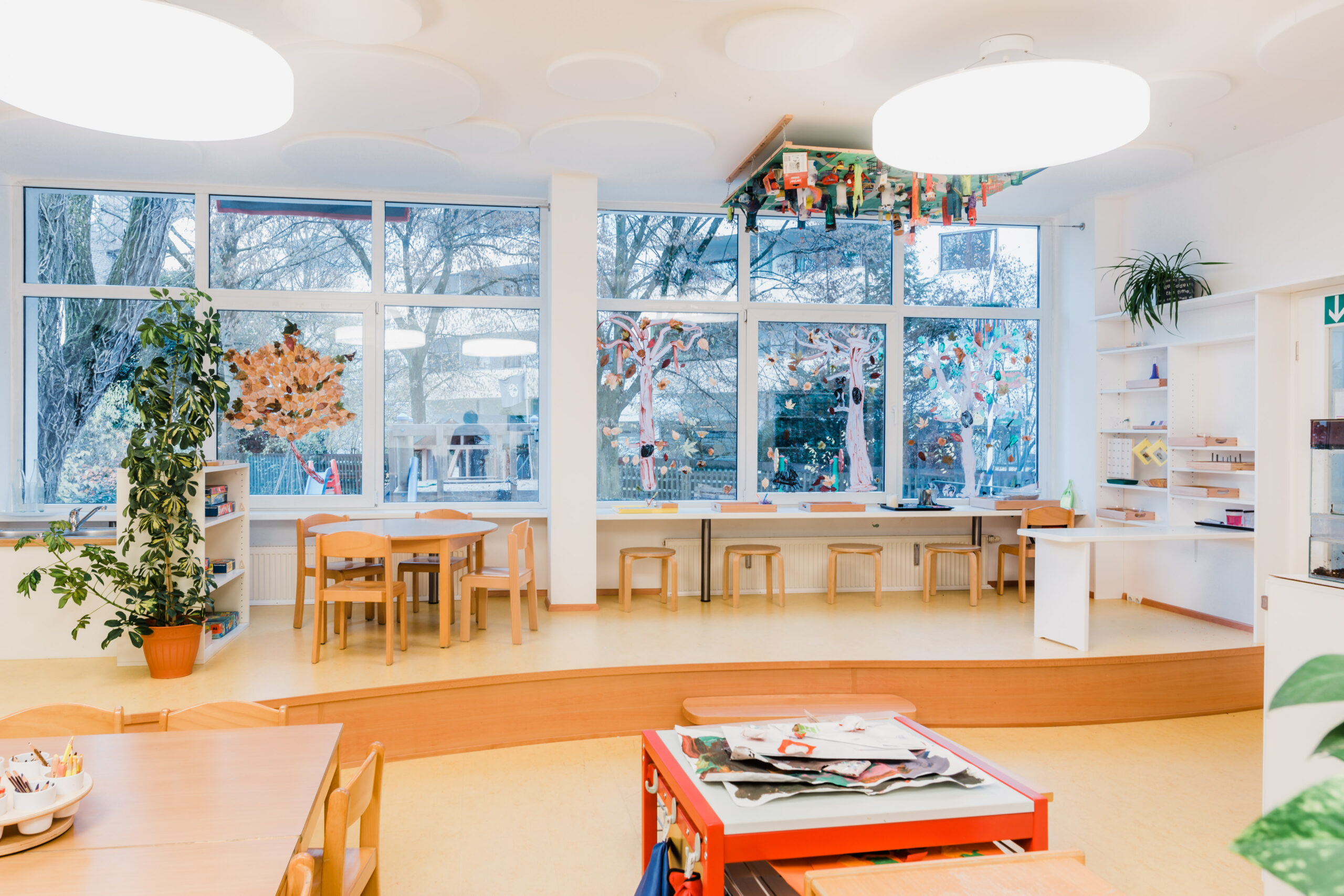 Heller Gruppenraum der Schmetterlinge mit großer Fensterfront, Tischen und Spielteppich