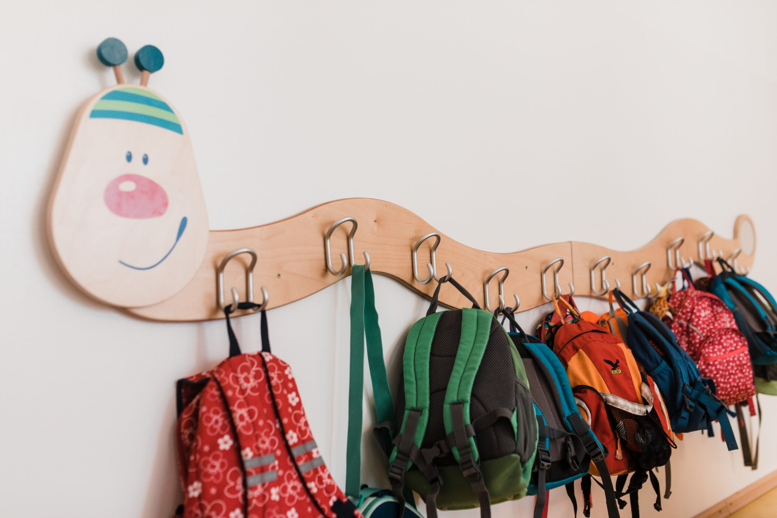 Garderobenhaken mit Kinderrucksäcken unter einer gemalten Raupe