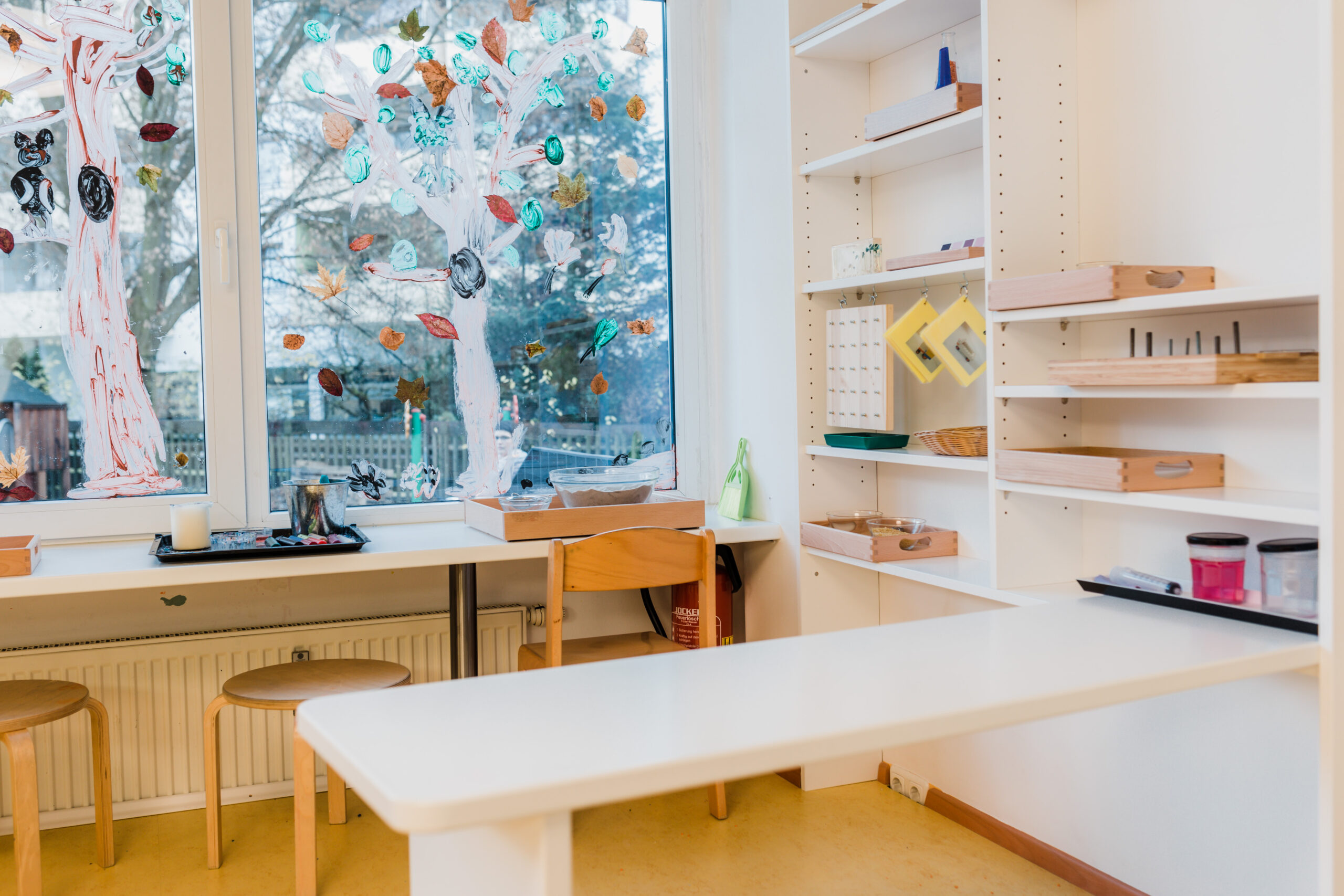 Langer Arbeitstisch am Fenster im Gruppenraum der Schmetterlinge mit Regalen und Materialien