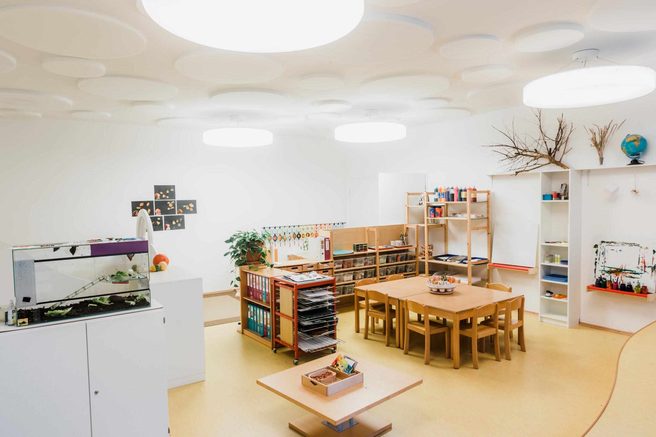 Gruppenraum mit Kindertischen, Regalen und Spielteppich